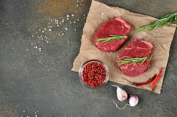 Two raw beef steaks on paper. Rosemary, garlic, pepper and grilled steak salt. Dark background. Top view. Free space for text.