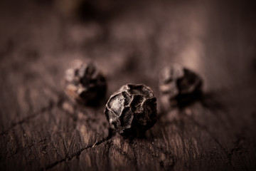 black pepper grains on wooden background close-up