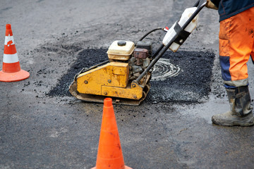 Construction worker in uniform operate vibratory plate compactor. Pothole repair process. Asphalt tamping machine operator. Pothole patching and repair. Laying asphalt around the hatch. New asphalt