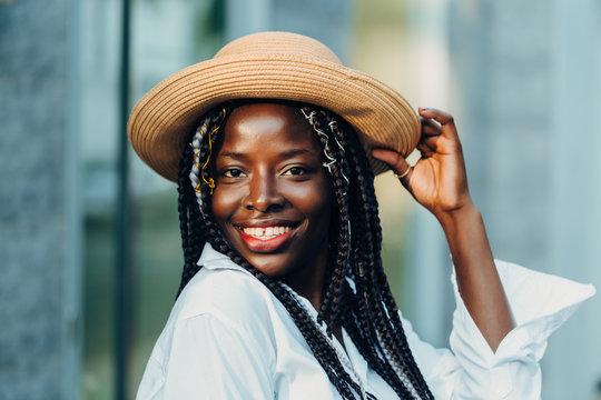 Portrait of a smiling young African American girl with pigtails in a hat walking down the street on a sunny day.