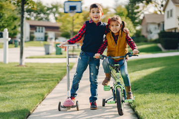 Obraz premium Brother and sister in a park. Boy with scooter. Girl with bicycle.