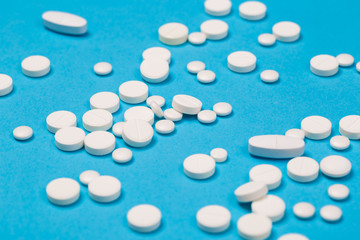 White Pills are scattered over a blue background. Close up. Medical background.