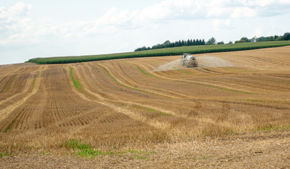 a tractor on which a trailer filled with liquid manure hangs drives over a field and sprays the liquid slurry