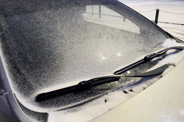 Car windshield in the snow in the evening under the light of a lantern