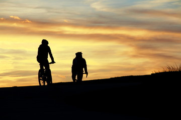 Silhouette of bike riders at sunset as they go over the hill.