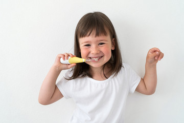 A girl in a white T-shirt brushes her teeth with an electric brush. Cute girl on a light background...