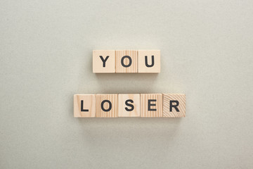 top view of wooden blocks with you loser lettering on grey background, bullying concept