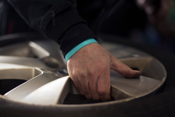 Man changing car tires in garage because of winter season. Workplace environment in dark colors, fitting the tire on rim.