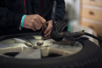 Obraz premium Man changing car tires in garage because of winter season. Workplace environment in dark colors, adjusting air pressure