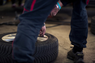 Man changing car tires in garage because of winter season. Workplace environment in dark colors,...