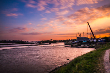 Sunset image along the bank of the river Deben with Melton boatyard in the background. The sky is a warm pastel colour