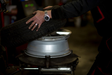 Man changing car tires in garage because of winter season. Workplace environment in dark colors, fitting the tire on rim.