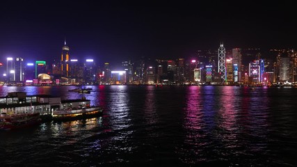 Nice night view of Victoria Harbour and Hong Kong Island from land side, Star ferry pier seen on left side. Bright illuminated towers, famous city skyline glow at dark hour, reflecting at harbor waves