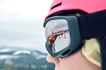 Close up portrait of snowboarder woman at ski resort wearing helmet and goggles with reflection of...