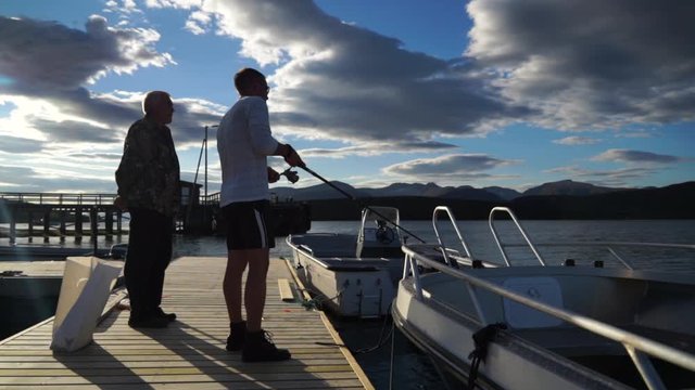 Two fishermen on pier boat dock in Tromso Norway in summer fishing for cod and haddock fish above Arctic Circle