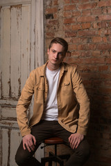 Sad and thoughtful young guy sitting on a chair. In the background is an old brick wall. Beautiful, expressive portrait made in the Studio in the loft design.