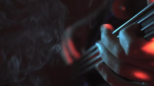 A guitarist performing bass party on electric fretless bass guitar turns around under warm lighting, with smoke