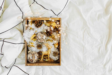 Set of Christmas decorations in wooden box on white bed with a blanket. Holiday concept. Flat lay, top view