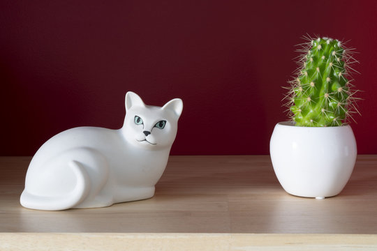 a white ceramic cat and small cactus on a shelf with a red wall