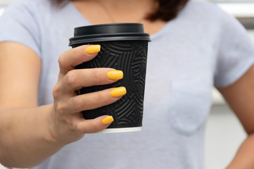 Female hand holding black paper cup with coffee to go