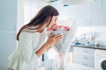 Woman smelling bouquet of roses. Housewife enjoying decor and interior of kitchen. Sweet home