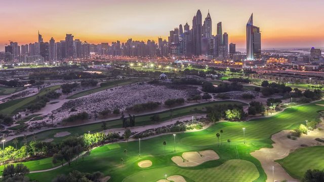 Jumeirah lake towers and Dubai Marina skyscrapers and golf course day to night transition timelapse, Dubai, United Arab Emirates. Aerial view from Greens district after sunset
