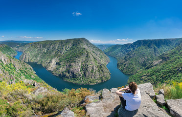 Fototapeta premium A woman contemplates the incredible Sil Canyon in the Ribeira Sacra from a fabulous viewpoint where she can see a meander of the Sil river