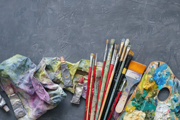 Artist paint brushes, palette, palette knifes, paint tubes on gray concrete background.