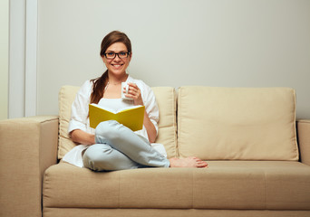 woman wearing glasses sitting on sofa and reading book.
