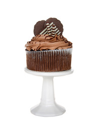 Giant chocolate cup cake with chocolate frosting, candy and cookies embellishing sitting on a white pedestal isolated on white.