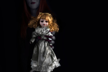 Hands of a witch with long sharp claws holding a creepy dirty porcelain doll. Halloween, black magic concept.