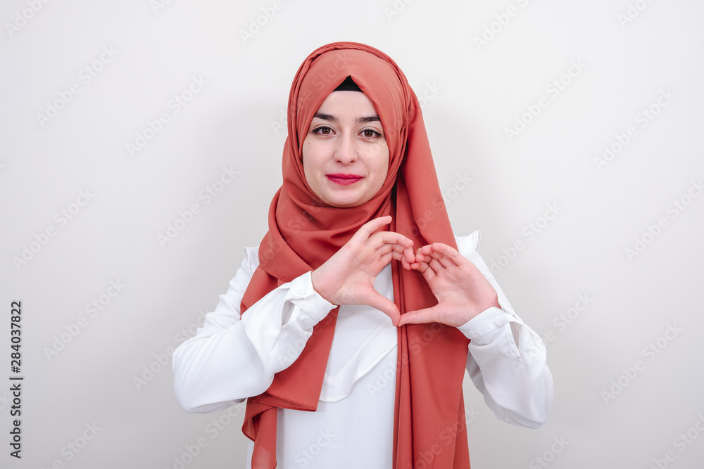 Wall mural Young hijab muslim woman making a heart gesture with her fingers, muslim girl gesture love heart sign