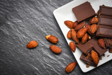 chocolate bar with almonds nut on white plate on the dark background - chunks candy sweet dessert and snack
