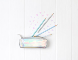 Holographic pencil case with pencils and heart confetti on white wooden background