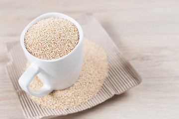 White cup filled with quinoa grains on wooden background