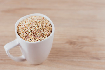 White cup filled with quinoa grains on wooden background