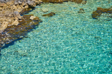 Fototapeta na wymiar Turquoise surface of waving water in sunshine on tropical rocky beach in Crete, Greece. Copy space.