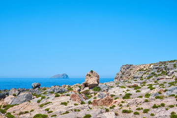                            Rocky seacoast with island on a background on a horizon with clear blue sky in Crete, Greece.    