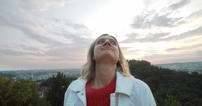 Outdoor portrait of stupid looking blonde girl making funny faces having fun time while staying on hills after sunset. Yong woman playing the ape on camera.