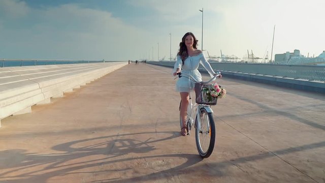 Beautiful Asian model in a blue dress rides a white bicycle on sea terrace in a modern city. Concert of travel, business and health