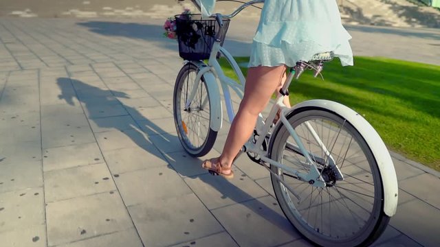 Beautiful Asian model in a blue dress rides a white bicycle in a green park with palm trees. Concert of travel, ecology and happiness