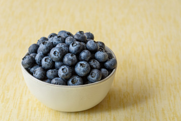 Fresh blueberries in a white ceramic bowl on a yellow crackle background