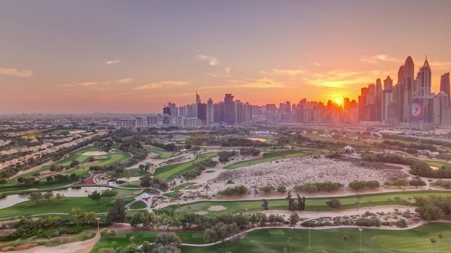 Dubai Marina and JLT skyscrapers and golf course sunset timelapse, Dubai, United Arab Emirates. Aerial view from Greens district. Rays of light and orange sky