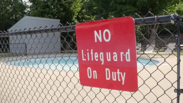 'No Lifeguard on Duty Sign' at a public pool. Bright red warning sign at a kiddie pool warns that there is nobody lifeguarding the area. Handheld shot depicts swimming at your own risk, safety issues.