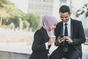 Muslim Businessman and businesswoman partner discussing using smartphone connection for work. Outdoor Setting.