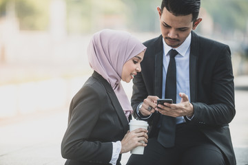 Muslim Businessman and businesswoman partner discussing using smartphone connection for work. Outdoor Setting.