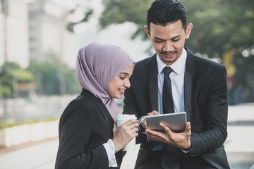 Muslim Businessman and businesswoman partner discussing using tablet for work. Outdoor Setting.