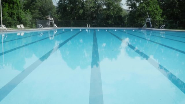Tilt to reveal a deserted outdoor olympic size swimming pool. The empty training pool waits for swimmers to arrive and start training. Low angle represents budget cuts, funding shortages and athletes 