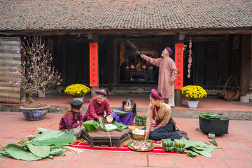 Vietnamese family members making Banh Chung together on old-styled house yard. Chung cake is a very...