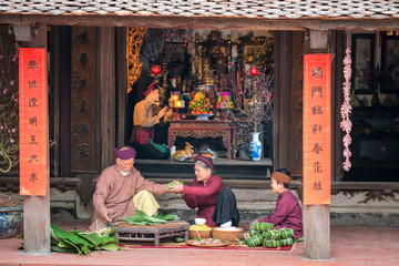 Vietnamese family members making Banh Chung together on old-styled house yard. Chung cake is a very...